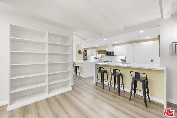a room with stainless steel appliances kitchen island granite countertop a table chairs cabinets and wooden floor