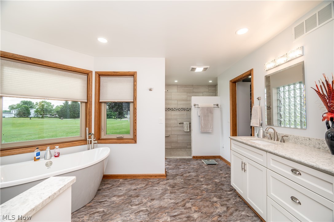 405 Airport Road Northwest Warren, OH 44481 - Photo 25 of 50 Freestanding soaking tub with a floor-mounted faucet, wood-finish window trim, double vanity with white cabinetry, light-toned countertop, and a tiled shower stall