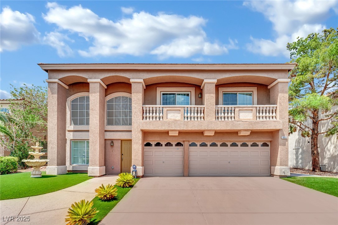 View of front facade featuring stucco siding, a balcony, driveway, and an attached garage