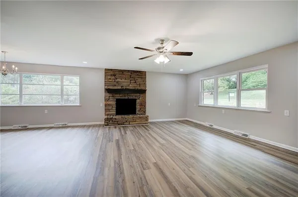 an empty room with wooden floor chandelier fan and windows