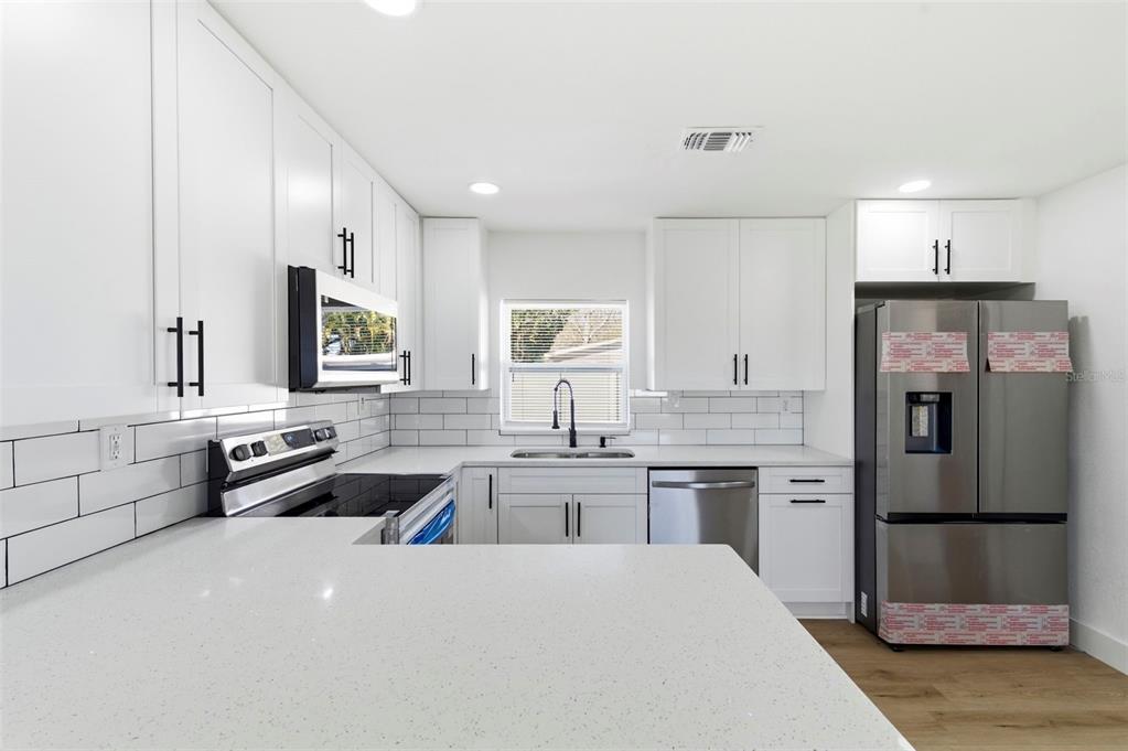 1448 South Belcher Road Largo, FL 33771 - Photo 11 of 47 a large kitchen with stainless steel appliances a stove a sink dishwasher a refrigerator and white cabinets with wooden floor