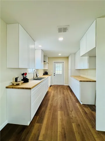 a large white kitchen with granite countertop a sink and dishwasher a stove top oven with wooden floor