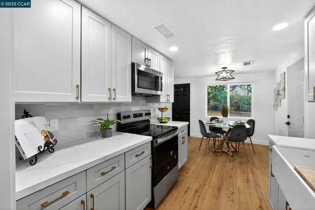 a kitchen with stainless steel appliances a white stove top oven a sink dishwasher a dining table and chairs with wooden floor