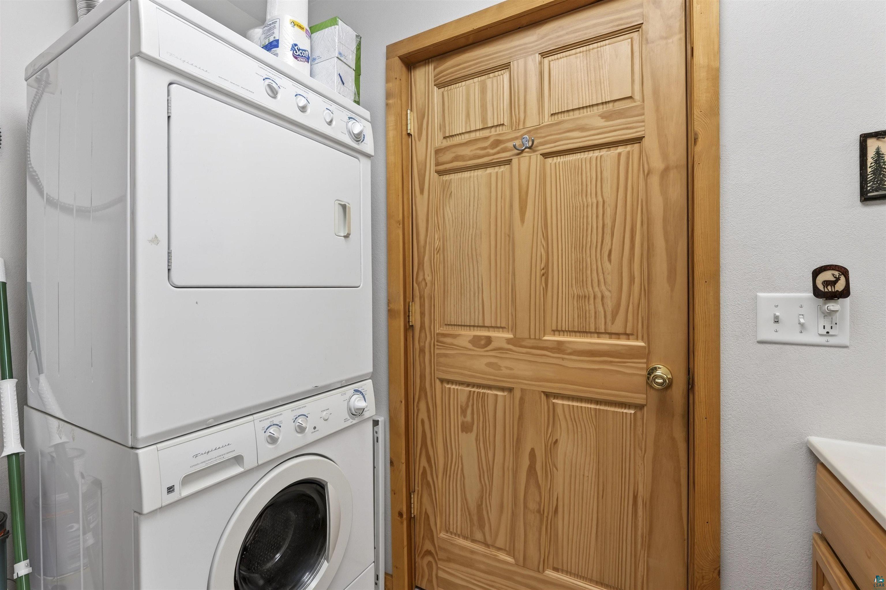 12235 East Crooked Lake Road Gordon, WI 54838 - Photo 26 of 48 Dedicated laundry area featuring a stacked washer and dryer, adjacent to a paneled wood door with a brass-finish doorknob