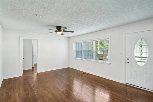 an empty room with wooden floor chandelier fan and windows