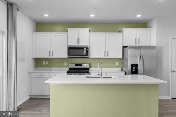 a kitchen with stainless steel appliances a stove a sink a microwave a refrigerator and white cabinets
