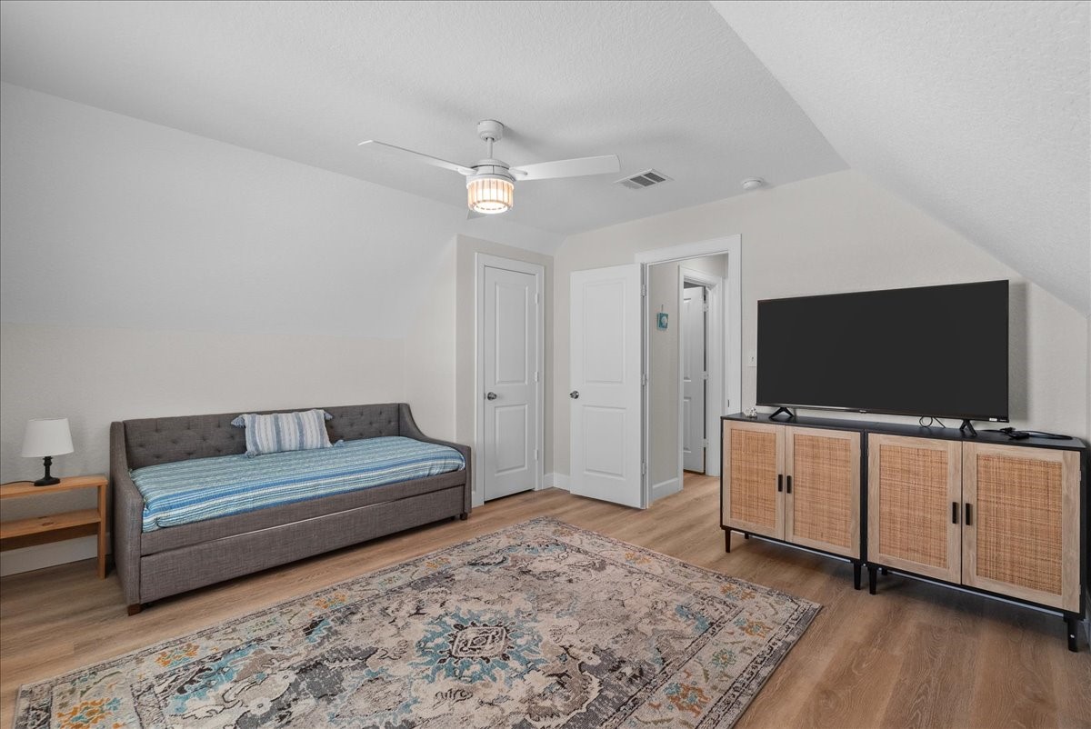 130 Beachcomber Avenue Surfside Beach, TX 77541 - Photo 20 of 33 This cozy bedroom features a daybed with a side table and lamp, a large TV on a modern console, and a stylish area rug. The room has a neutral color palette and a ceiling fan, providing a comfortable and inviting space.