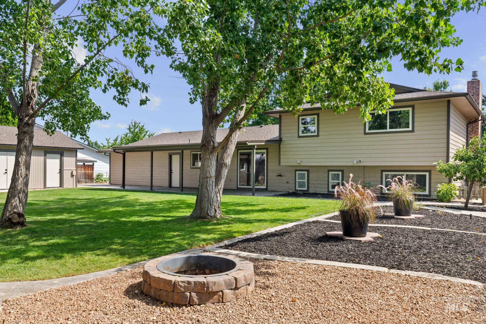 1675 Country Terrace Way Meridian, ID 83642 - Photo 41 of 50 Expansive backyard featuring a stone-clad fire pit, decorative rock landscaping, a manicured lawn, and mature trees