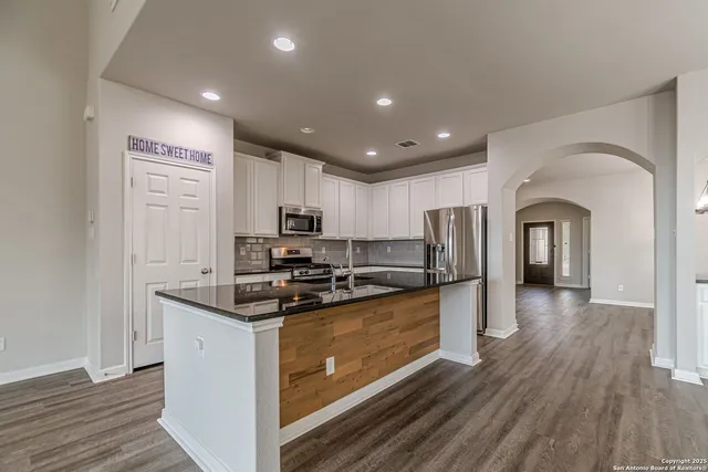 a large kitchen with stainless steel appliances granite countertop a stove a refrigerator a sink a microwave oven a large island with wooden floor and cabinets