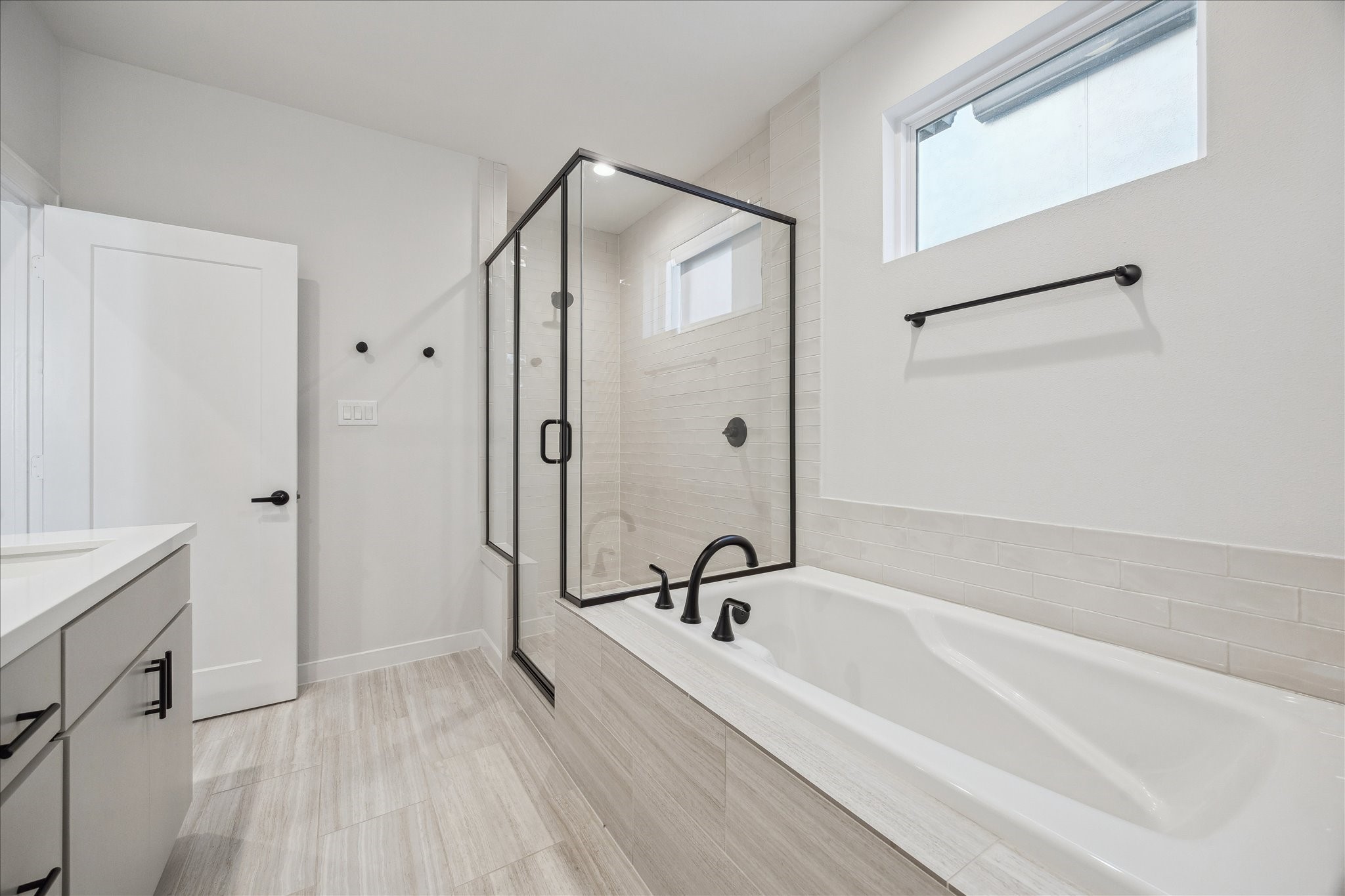 1603 Patterson Street, Unit E Houston, TX 77007 - Photo 29 of 32 This photo showcases a modern bathroom with a sleek glass-enclosed shower and a spacious bathtub. The room features neutral tones, stylish fixtures, and ample natural light from a small window, creating a clean and inviting atmosphere.