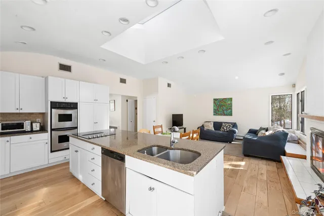 a white kitchen with stainless steel appliances granite countertop a sink dishwasher stove top oven and refrigerator with wooden floor