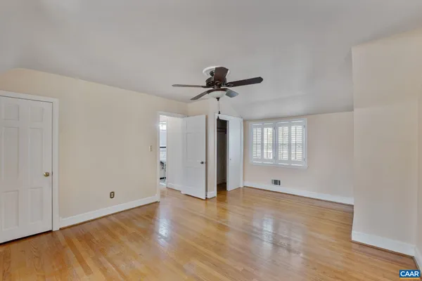 a view of an empty room with wooden floor and a ceiling fan