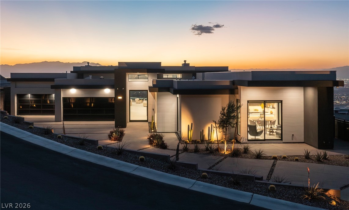 563 Grand Rim Drive Henderson, NV 89012 - Photo 41 of 70 Modern architecture glows at dusk, showcasing desert landscaping and a distant city view.