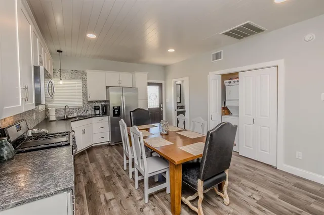 a kitchen with stainless steel appliances granite countertop a stove top oven a refrigerator a sink and white cabinets with wooden floor