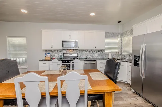 a open kitchen with stainless steel appliances granite countertop a stove top oven a sink dishwasher a dining table and chairs with wooden floor