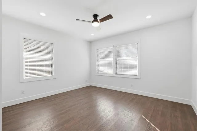 an empty room with wooden floor ceiling fan and windows