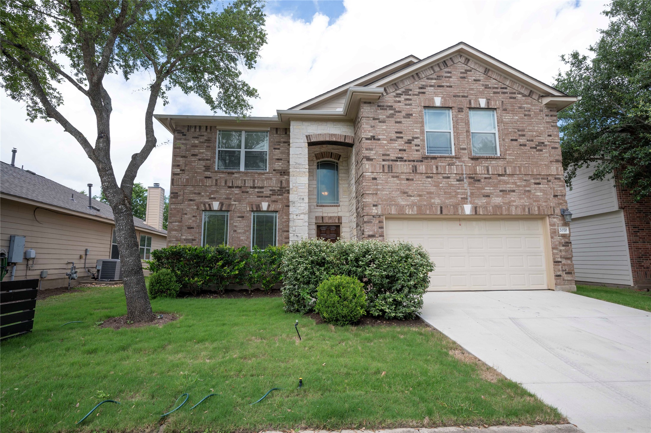 2070 Intrepid Drive Buda, TX 78610 - Photo 30 of 31 A classic brick exterior with a two-car garage awaits, framed by established trees and well-maintained shrubbery.