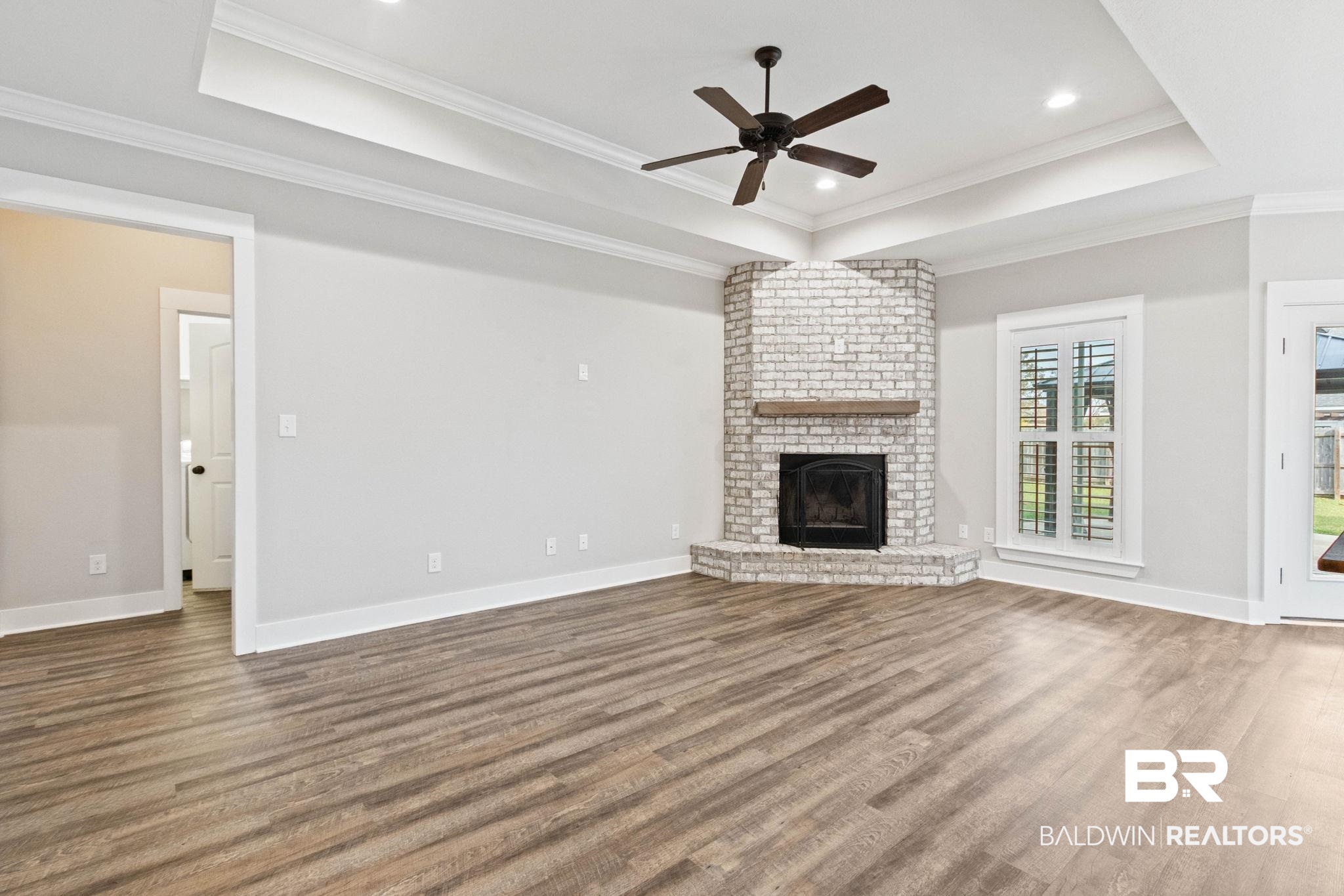 17376 Bankhead Boulevard Fairhope, AL 36532 - Photo 11 of 73 Unfurnished living room with a raised ceiling, crown molding, ceiling fan, a fireplace, and wood finished floors