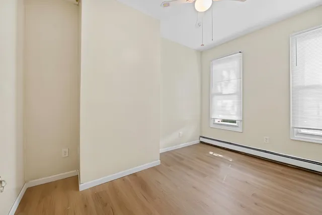 an empty room with wooden floor chandelier fan and windows