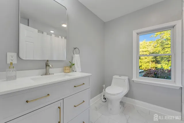 a bathroom with a toilet a sink a mirror a window and vanity