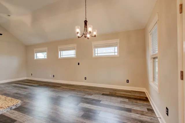 an empty room with wooden floor chandelier fan and windows
