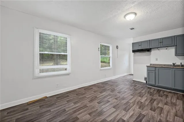 a view of a kitchen and an empty room with wooden floor and a window