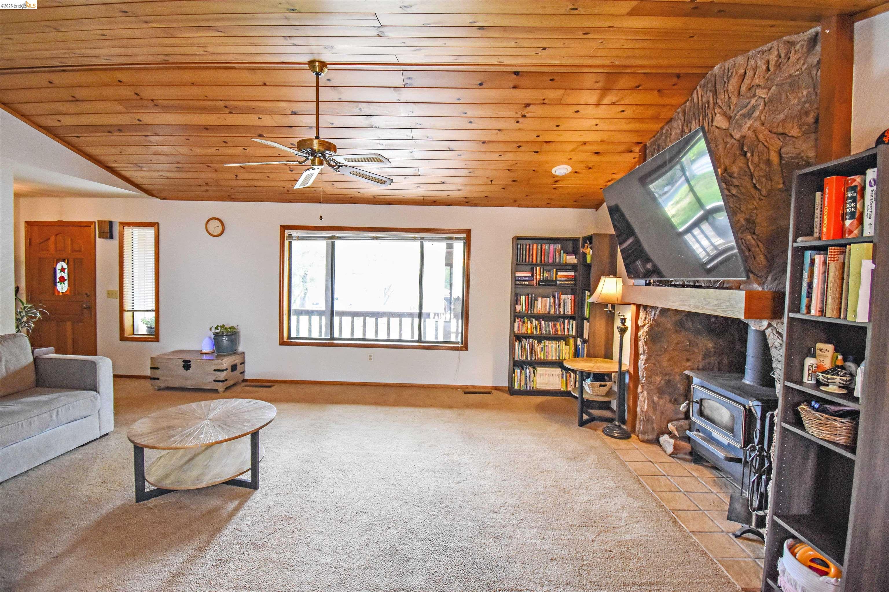 15 Roble Road Sonora, CA 95370 - Photo 11 of 44 Living area with a vaulted wooden ceiling, a wood stove, a ceiling fan, and light carpet