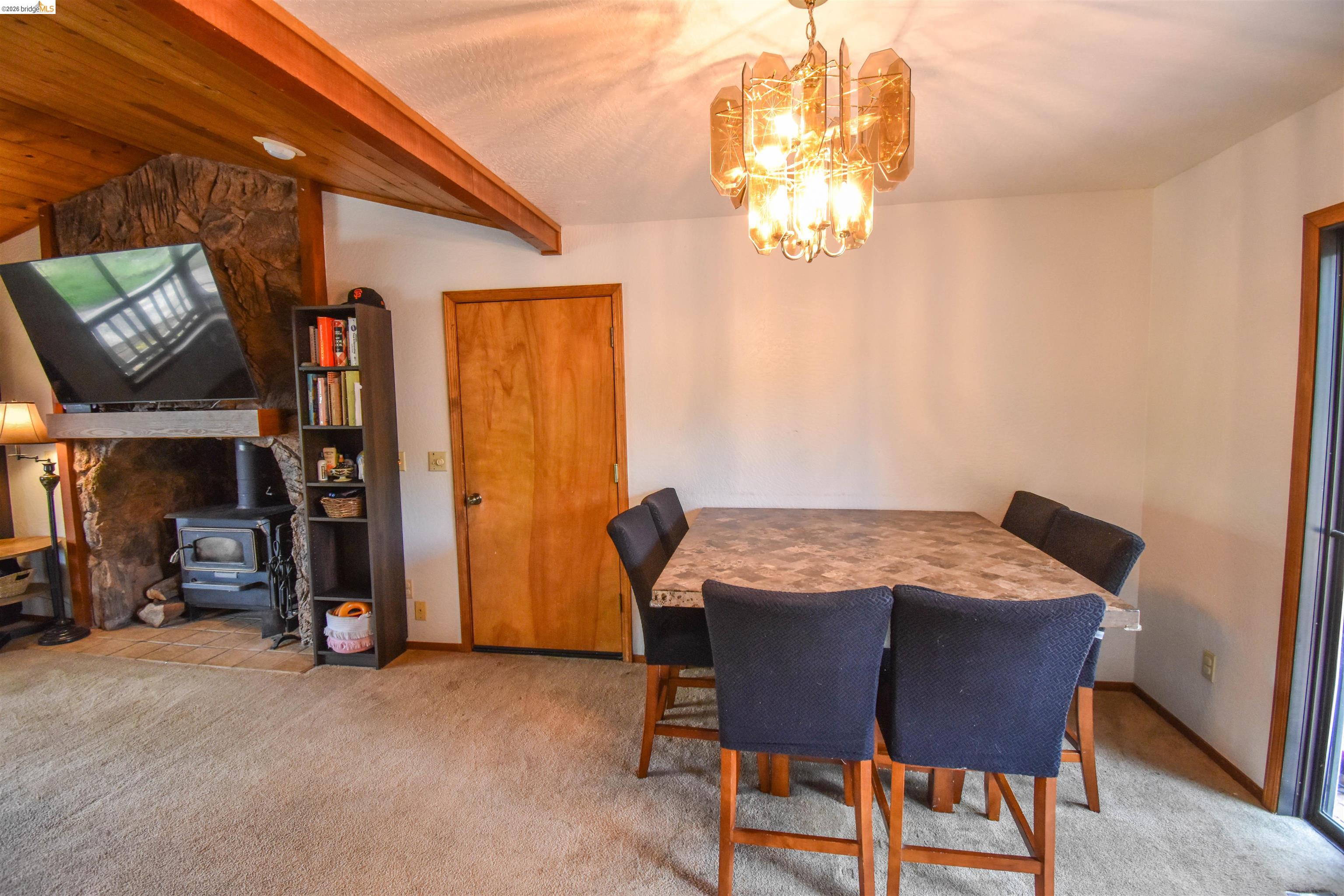 15 Roble Road Sonora, CA 95370 - Photo 12 of 44 Dining room featuring a wood stove, light colored carpet, suspended lighting, and lofted ceiling with beams
