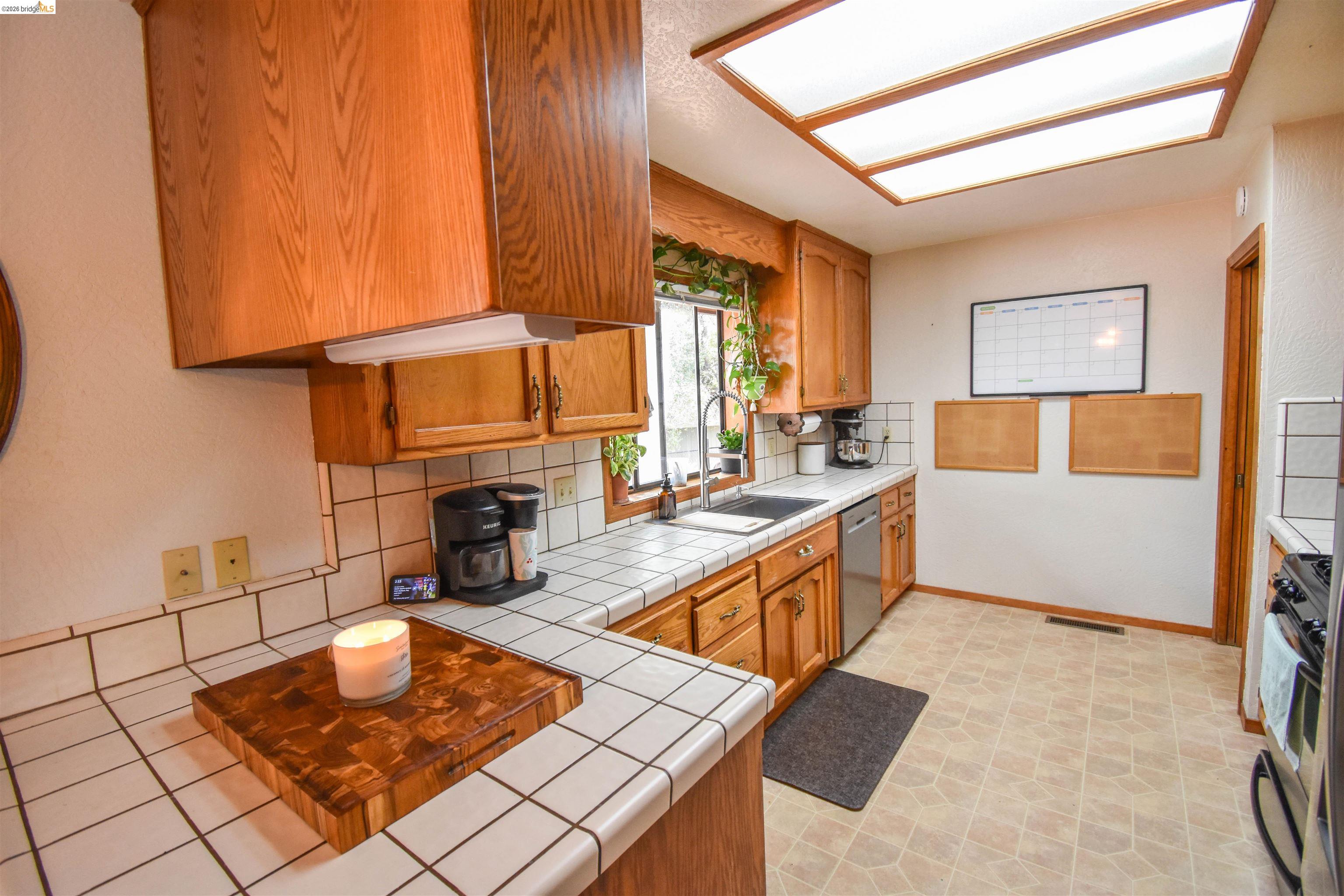 15 Roble Road Sonora, CA 95370 - Photo 14 of 44 Kitchen featuring tile countertops, wood finish cabinetry, tasteful backsplash, black range with gas stovetop, and dishwasher
