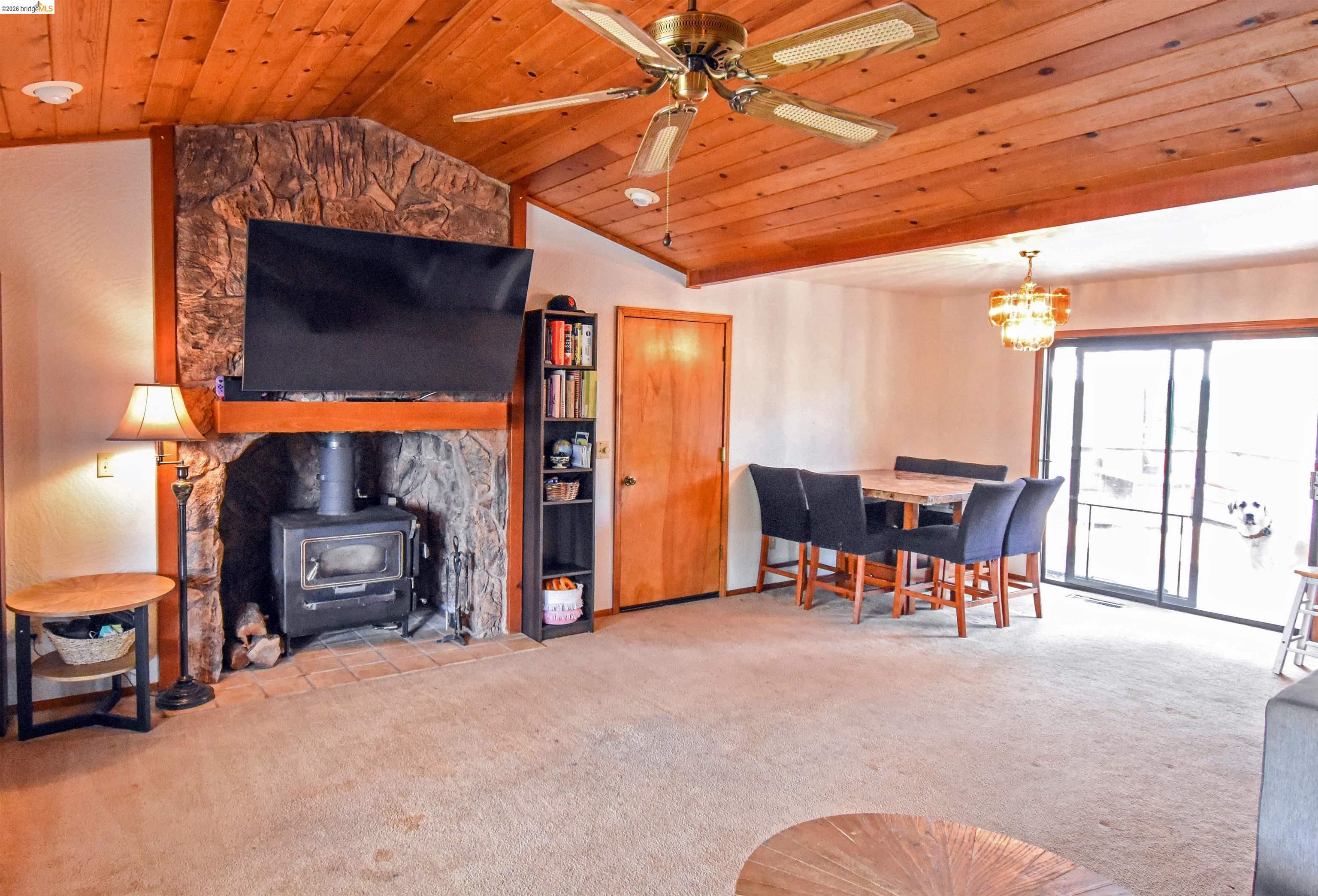 15 Roble Road Sonora, CA 95370 - Photo 9 of 44 Living room with a vaulted wood ceiling, a wood stove, light carpet, a ceiling fan, and a chandelier