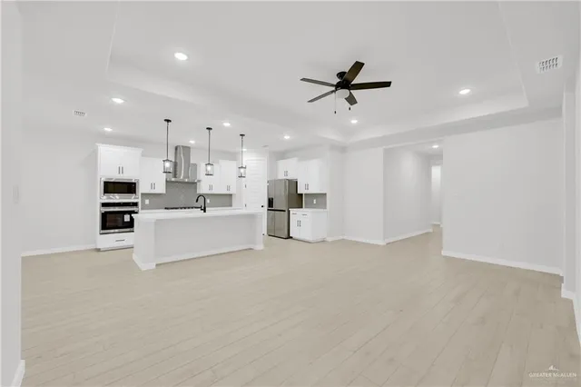 a large white kitchen with kitchen island a stove a sink a refrigerator and white cabinets with wooden floor