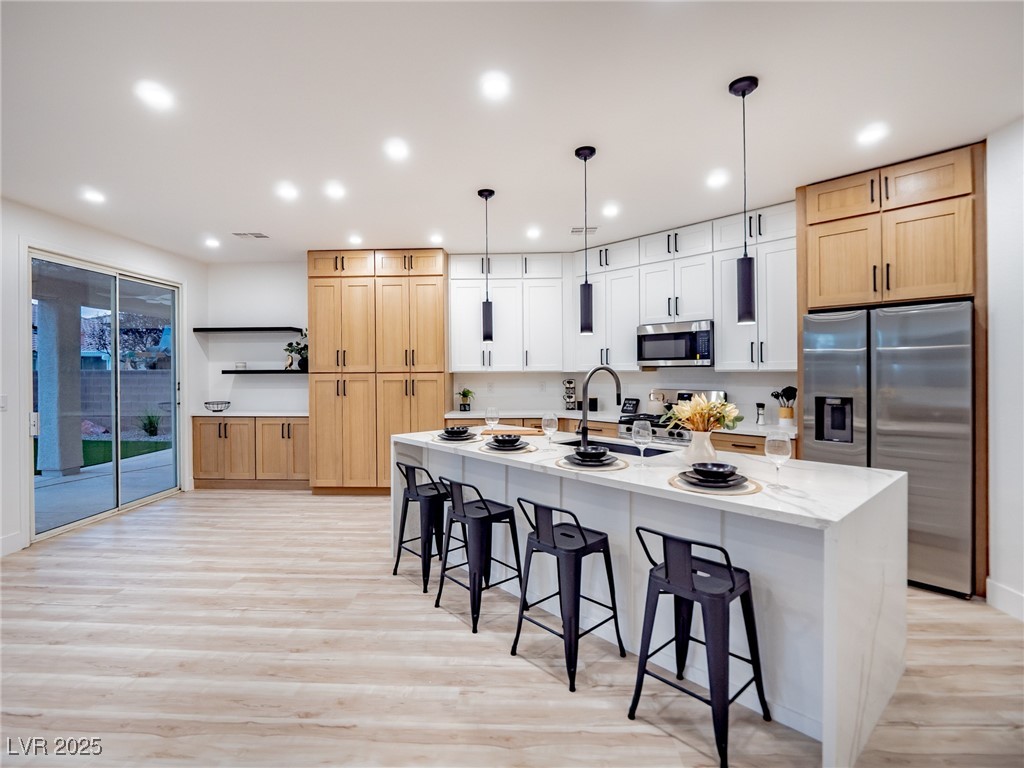 7870 Midnight Ride Street Las Vegas, NV 89131 - Photo 3 of 69 Kitchen with a kitchen bar, stainless steel appliances, light wood finished floors, light stone countertops, and recessed lighting