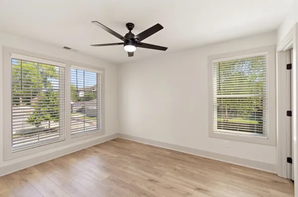 a view of a big room with wooden floor a ceiling fan and windows