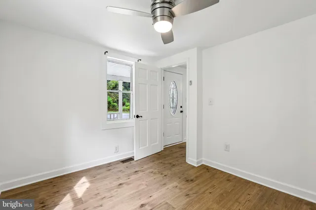 an empty room with wooden floor ceiling fan and window
