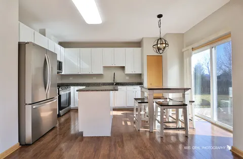 a kitchen with stainless steel appliances granite countertop a refrigerator a stove top oven a sink and white cabinets with wooden floor