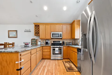 a kitchen with stainless steel appliances granite countertop a refrigerator a sink dishwasher a stove and a sink with wooden floor