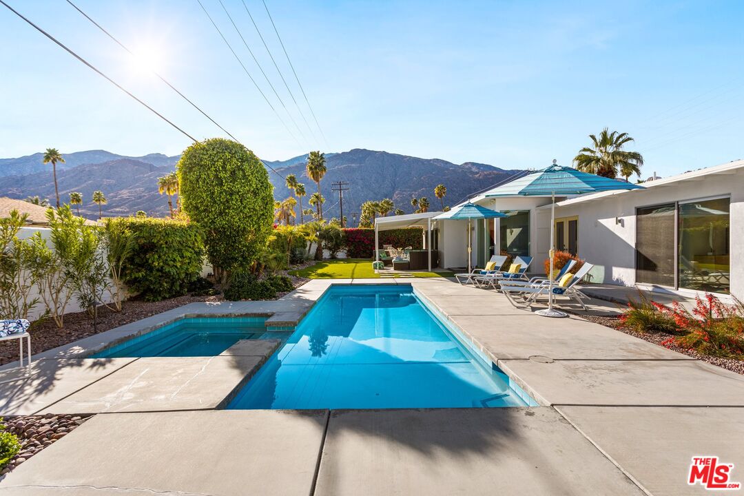 975 East Sunny Dunes Road Palm Springs, CA 92264 - Photo 28 of 40 a view of a white house with swimming pool lawn chairs and wooden fence