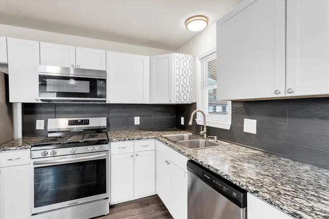 a kitchen with granite countertop a sink stainless steel appliances and white cabinets
