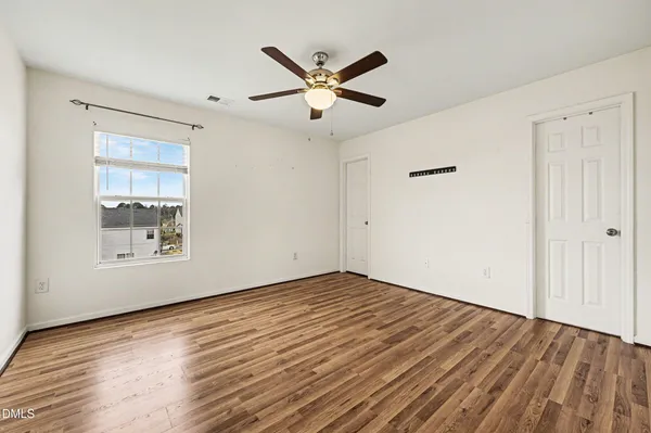 a view of an empty room with wooden floor and a ceiling fan