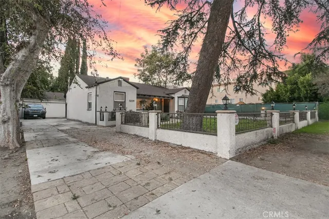 a view of a white house next to a yard with road and trees