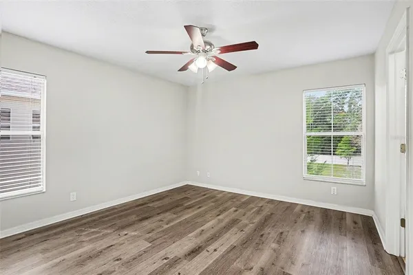 an empty room with wooden floor fan and windows