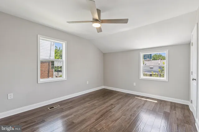 an empty room with wooden floor ceiling fan and windows