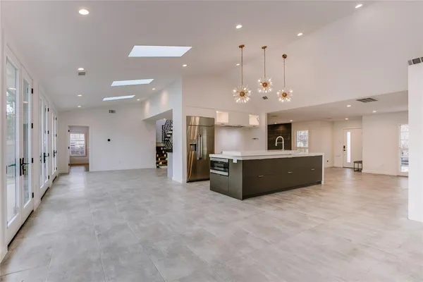 a large hall with stainless steel appliances kitchen island a large counter top and a chandelier
