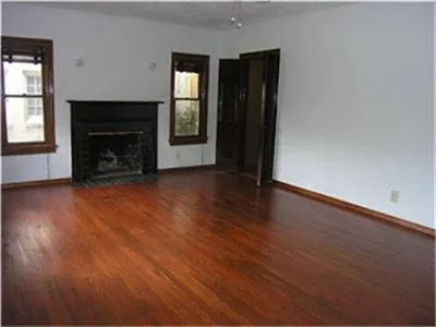 an empty room with wooden floor fireplace and windows