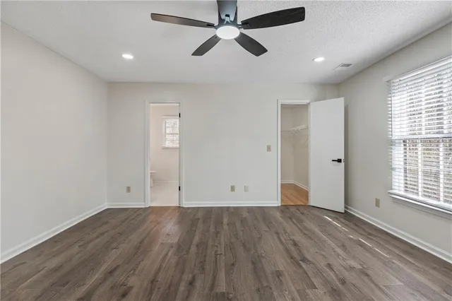 an empty room with wooden floor ceiling fan and windows