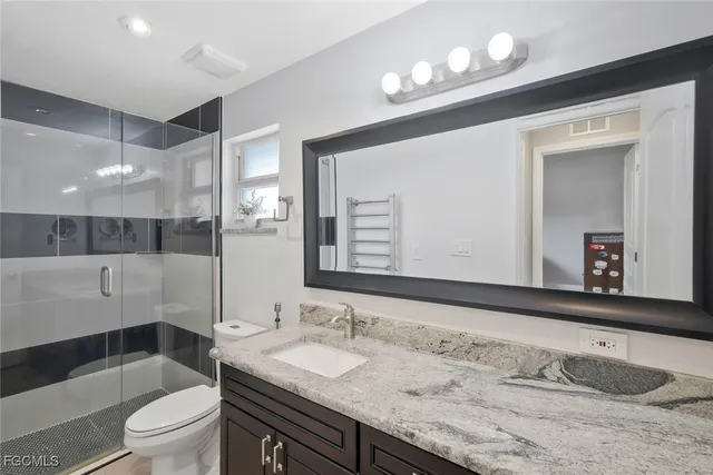 a bathroom with a granite countertop sink a toilet a mirror and shower