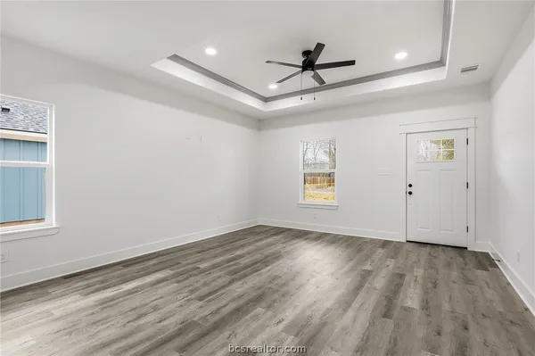 an empty room with wooden floor ceiling fan and windows