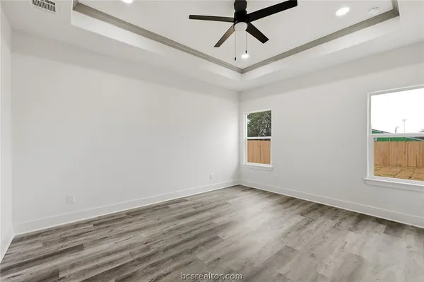 an empty room with wooden floor ceiling fan and windows