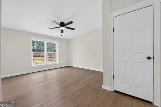 an empty room with wooden floor ceiling fan and windows