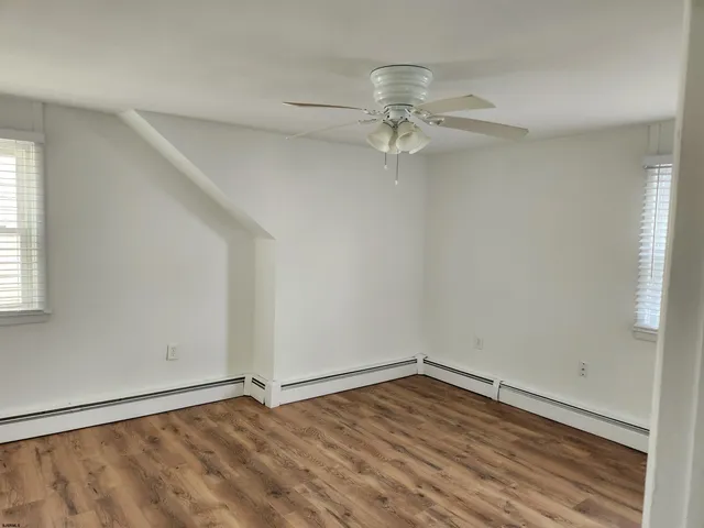an empty room with wooden floor chandelier fan and windows